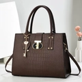 Detail of dark brown faux crocodile handbag featuring a golden T-lock and heart pendant - Coffee