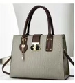Close-up of crocodile textured gray leather bag with dark brown handles and golden lock - Gray