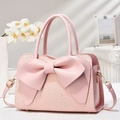 Pink bow handbag with woven texture and gold hardware on a minimalist white desk - Pink
