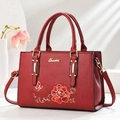 Detail einer roten Handtasche aus Leder mit Blumenstickerei und goldenem Logo-Akzent - Burgunderrot