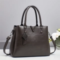 Detalle del bolso de cuero con textura, herraje metálico en V y colgante elegante - Gris