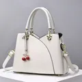 Borsa a mano bianca in pelle con profili neri, fibbia dorata e ciondolo a ciliegia su podio - Bianco Sporco