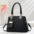 Elegante schwarze strukturierte Makronen-Handtasche mit goldener V-Verzierung auf weißem Sockel - Schwarz