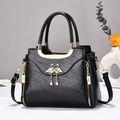 Elegant black leather handbag with gold swan buckle and pearl charm, shown in a lifestyle set - Black