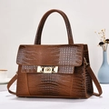 Detail of dark brown crocodile embossed handbag featuring a golden metal twist lock closure - Earthy Yellow