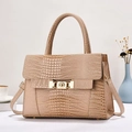 Elegant beige crocodile pattern handbag with gold clasp shown in a lifestyle setting - Khaki