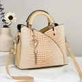 Detail der aprikosenfarbenen Handtasche mit Krokodilprägung und einem Herz-Perlenanhänger - Beige