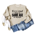 Nahaufnahme des beigen Rundhals-Sweatshirts mit künstlerischem 'It's so weird' Text - S / Sandfarben (Schwarze Schrift)