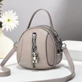 Detail view of grey litchi leather round bag featuring silver bear charm and metal tassel - 17x8x18 / Light Gray