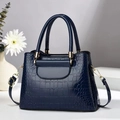 Detail der blauen Handtasche mit Krokodilmuster, goldener Hardware und abnehmbarem Gurt - Saphirblau