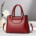 Close-up of red crocodile-embossed leather handbag with gold hardware and top handles - Wine Red