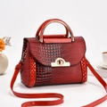 Detail showing red faux crocodile leather texture and golden twist lock on handbag - Red