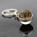 Macro shot of Bigfoot glass dome keychain with I Never Look Good In Photos text - Sitting Bigfoot in Forest (JY007426-8)
