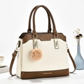 Detail view of two-tone litchi grain shoulder bag with plush ball charm on a studio desk - Off White