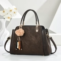 Bolso de mano en cuero marrón oscuro con pompón de pelo y bandolera sobre fondo blanco - café
