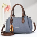 Detail of blue denim handbag featuring brown leather trim and colorful beaded tassel charm - Blue