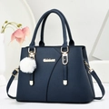 Minimalist navy blue leather handbag with gold hardware and plush charm on white stand - Blue