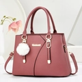Borsa a mano rosa con texture litchi, logo dorato e morbido pompon bianco su sfondo bianco - Rosa