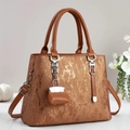 Detail of metallic bronze handbag texture with silver hardware and mini charm - Earthy Yellow