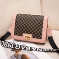 Pink printed crossbody square bag with gold lock and wide lettered strap on sofa - Pink