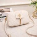 Elegant cream quilted crossbody bag with golden crown buckle and tassel on table - White