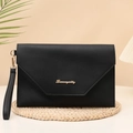 Sleek black faux leather envelope clutch bag with gold logo on a woven mat - Black