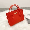 Elegant red litchi grain tote bag with gold metal plate on white plush carpet - Red
