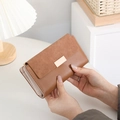 Dettaglio di un portafoglio lungo in pelle marrone con chiusura dorata in un set elegante - caffè