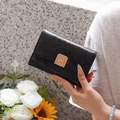 Detail of black pleated glossy wallet with golden metal clasp and decorative wrist strap - Black