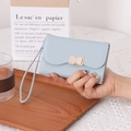 Light blue faux leather wristlet wallet with a gold bow buckle in a minimalist scene - Light Blue