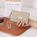 Macro detail of a beige trifold wallet with a gold bow buckle and wristlet strap - Green