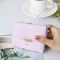 Close-up of lavender trifold wallet with golden leaf clasp and brand engraving - Purple