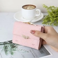 Pink trifold wallet with gold leaf clasp and quilted stitching held in hand - Pink
