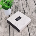 Detail der quadratischen Papier-Geschenkbox mit geometrischem Muster und Merci-Etikett - Wellenmuster-Stil