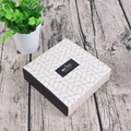 Detail der quadratischen Geschenkbox mit Y-Geometriemuster und Merci Beaucoup Etikett - Geometrisches Gitterstil