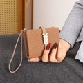 Detail of tan bifold wallet featuring knit texture embossing and a metal leaf buckle - Brown