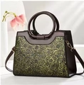 Details des geprägten Blumenmusters und der runden Griffe an einer braunen Ledertasche - Gold