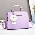 Close-up of lilac glossy bag with geometric embossing and white plush monster charm - Purple