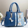 Dettaglio ricamo floreale su borsa blu con elegante ciondolo a fiocco e finiture in metallo oro - Blu
