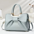 Elegante bolso de mano azul claro con lazo y asa metálica en un ambiente moderno - Azul Celeste