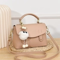 Detail of pink satchel featuring pebble texture with a plush cartoon charm on a woven mat - Apricot