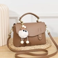 Brown lychee leather satchel bag with cute monster charm on woven mat tabletop - Khaki