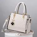 Detail of white handbag featuring geometric triangle pattern and gold clover pendant - Off White