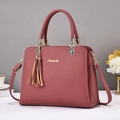 Pink lychee texture leather tote bag with gold hardware and tassel charm on a white desk - Pink