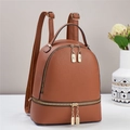 Nahaufnahme des braunen Lederrucksacks mit goldenen Reißverschlüssen und Schlossanhänger - 24x12x29cm / Erdgelb