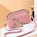 Pink crossbody bag with floral embroidery and gold zippers on white pedestal - Pink