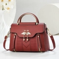 Detalle del bolso de cuero rojo vino con logo de cisne dorado y costuras en forma de V - Granate