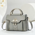 Macro detail of grey litchi leather bag with gold swan buckle and pearl charm - Gray