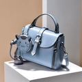 Light blue faux leather crossbody bag with a cute cat pendant on minimalist display - Blue