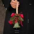 Christmas bell ornament with pine cones and red bow held against a black coat background - Style A Green